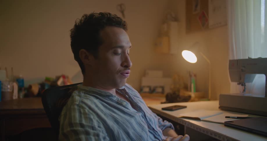Young man sitting in front of a sewing machine at home thinking