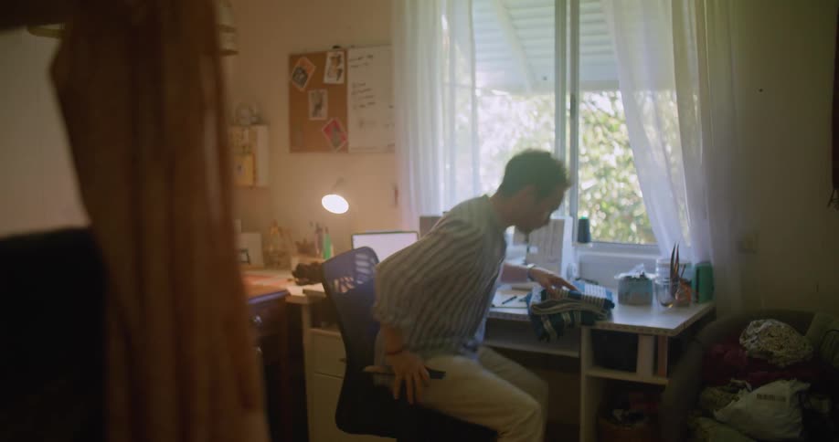 Young man working at home in a sewing studio picks up cloths from a shelf