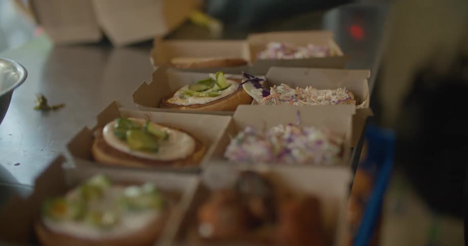 A restaurant employee adds toppings to burger buns in cardboard holders