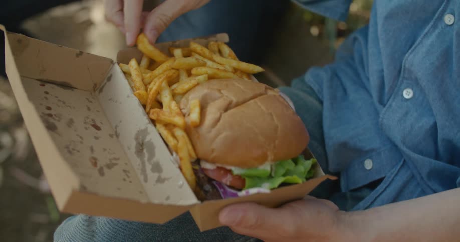 A person opens a box that has a cheeseburger and fries and another person reaches for a fry