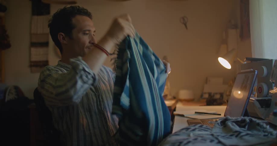 A man sits in a sewing room and shares fabric swatches with a woman on a video call