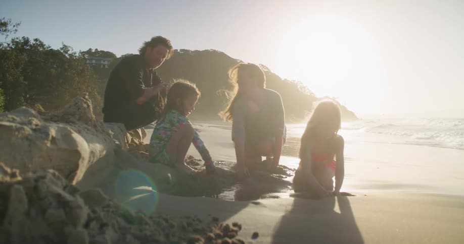 Family playing with sand on the beach next to the ocean at sunset