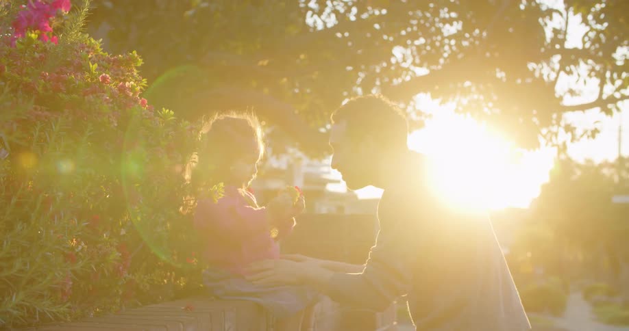 A man plays with a little girl sitting on a brick wall outside