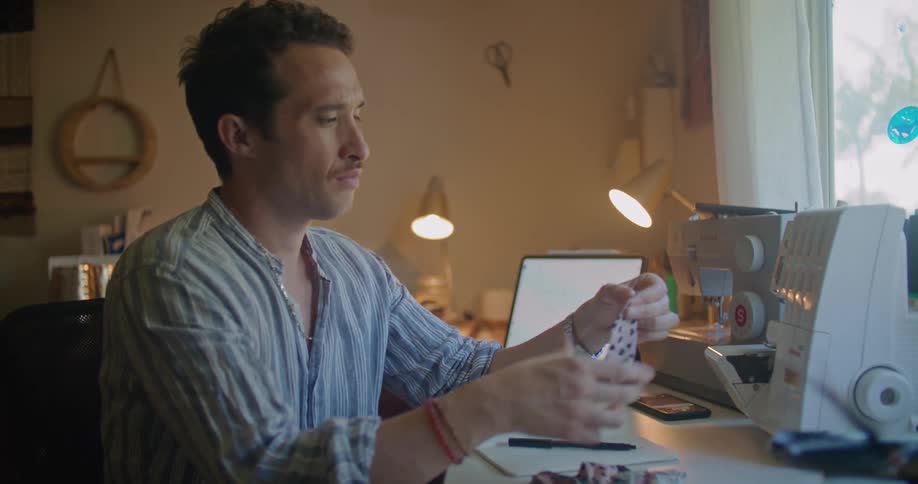 Man sitting next to sewing machine examines fabric pieces