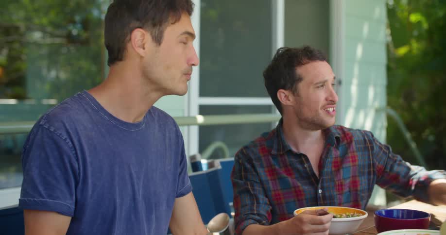 Two men eat and talk together outside