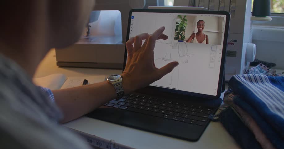 A man zooms in on a clothing design on a laptop while discussing with a woman on a video call