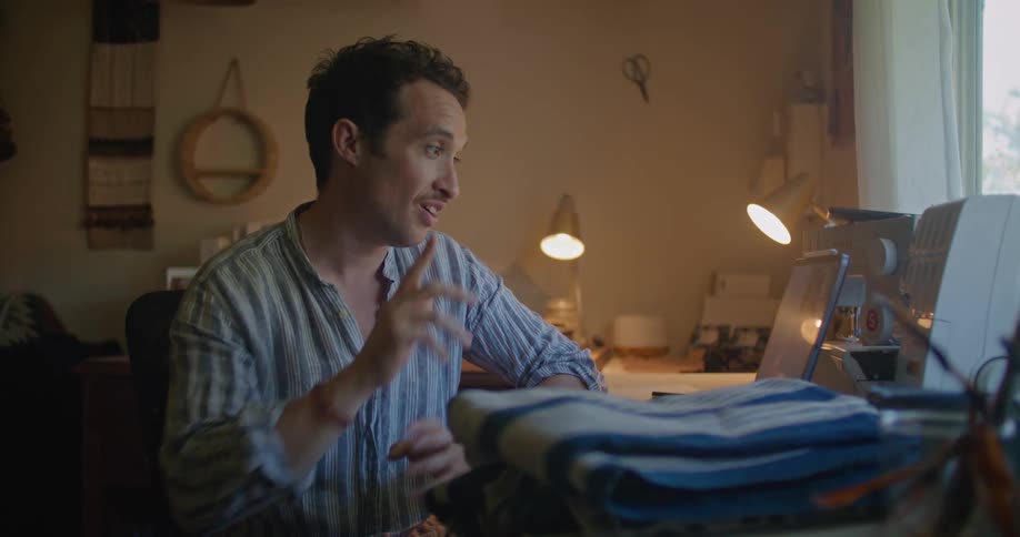 A man folds fabric while talking in his office on the tablet
