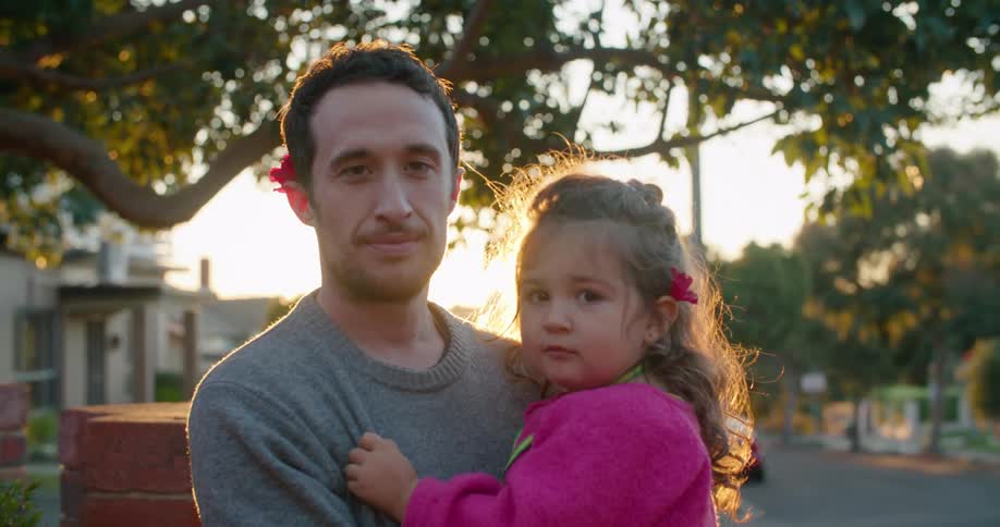 Man stands near street holding daughter and smiles