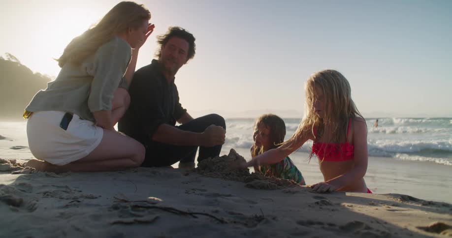 A family sit on the beach and the children build a sand castle