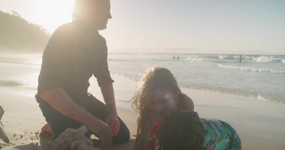 A father helps his children build a sand castle