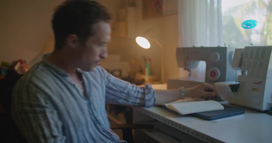 A man leaning back twirling his pen sits up and crumples a piece of paper in frustration