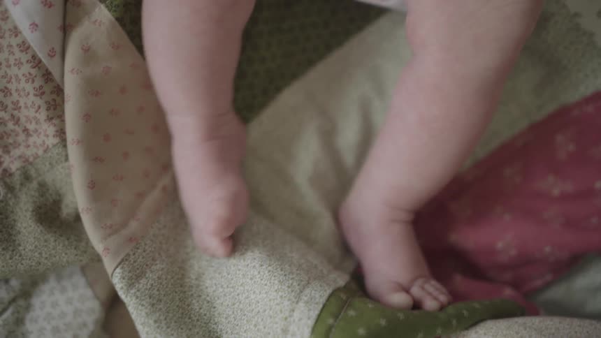 A baby kicks its feet while lying on a quilt