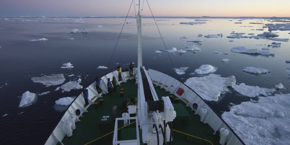 A large freight ship is moving past ice on either side
