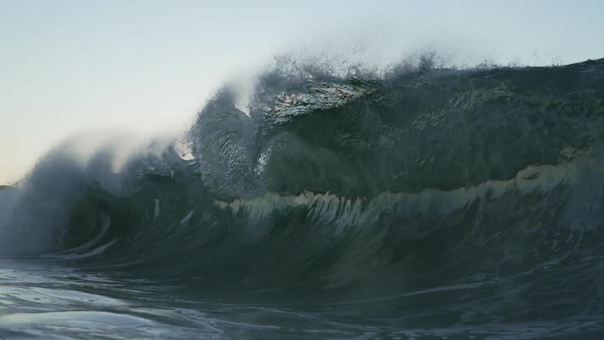 Large wave breaks against the shore at dusk