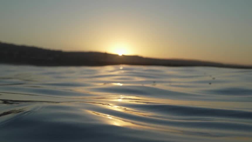 Waves roll in the ocean as a person swims as the sun sets