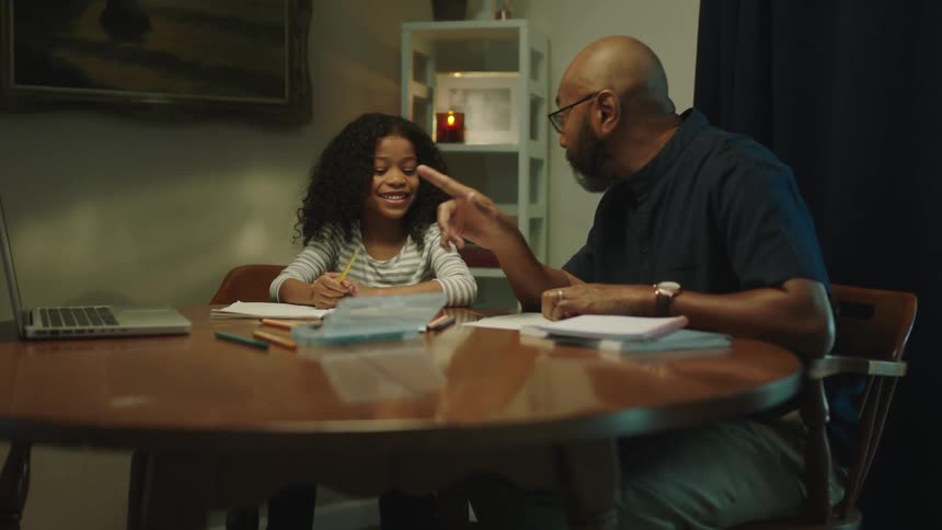 A girl smiles at her dad as he talks to her while working on schoolwork