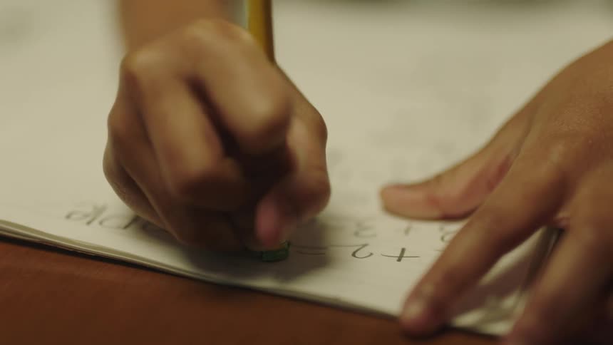 A childs hand holding a pencil erasing part of a math equation