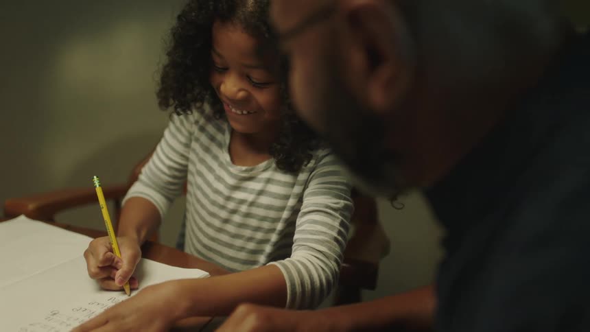 A girl laughs while working on homework with her father