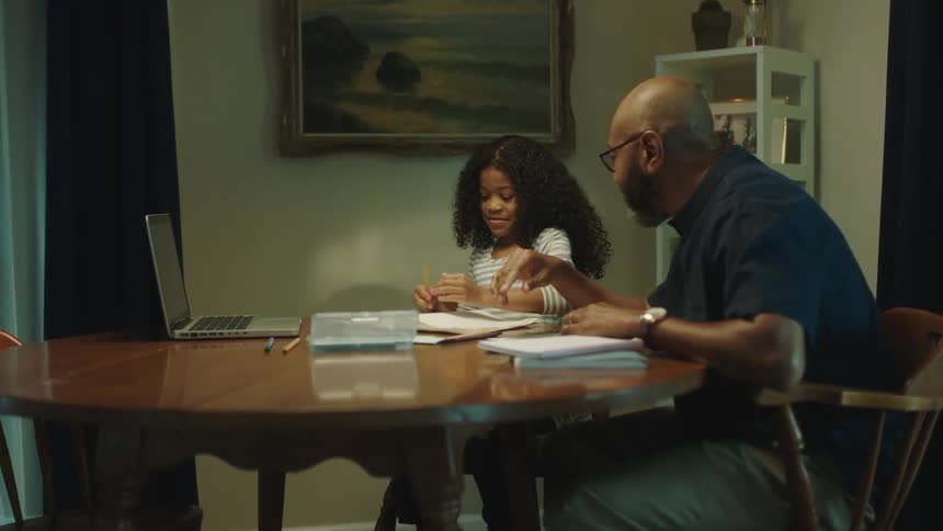 Father helping her daughter with homework sitting at the dinner table at home
