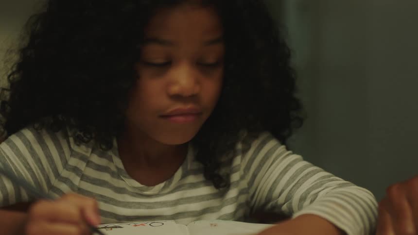 A little girl looks up from her school work as dad gives her a thumbs up
