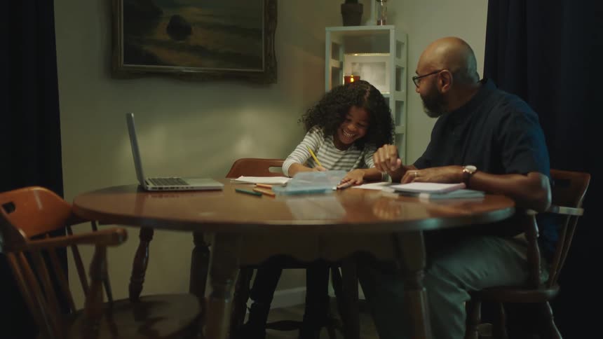 Father sitting at the dinning table at home helping his daughter with homework
