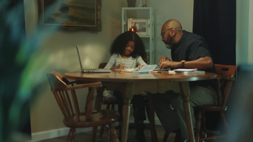 A father is helping his daughter do homework at the table