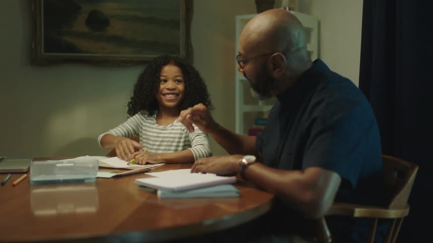 A man is helping a young girl with her homework and they highfive each other