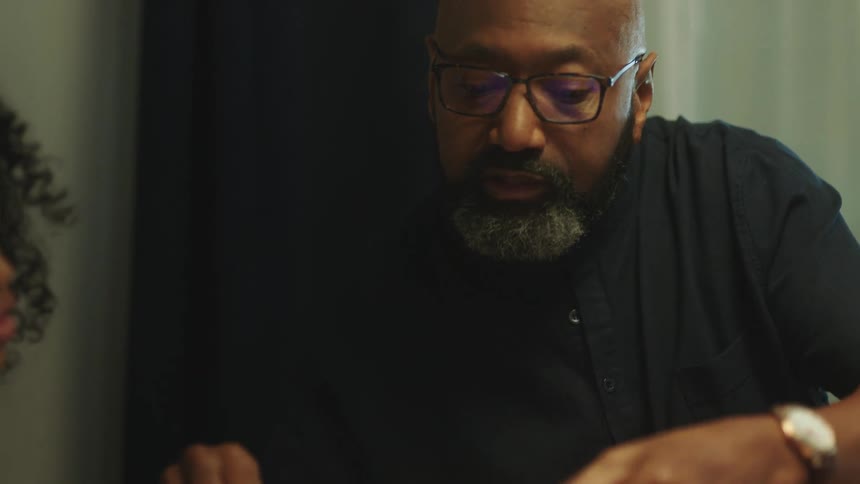 Bald teacher with glasses beard and black shirt teaches girl with curly hair