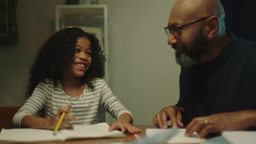 Father helps his daughter with homework sitting on the dinning table at home