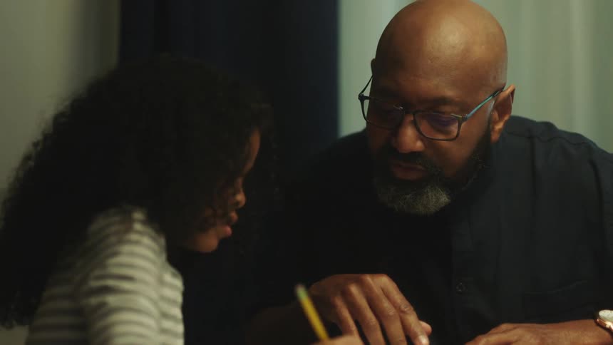 Father helps daughter with homework sitting at the dinning table at home