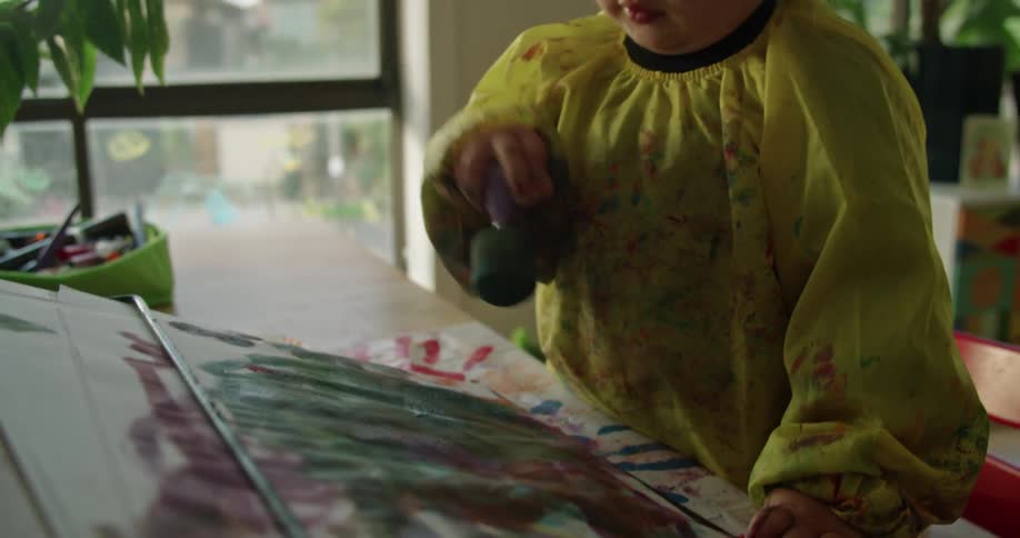A little girl is at a table painting on a paper