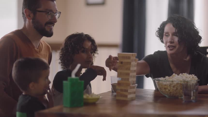 Family sits at table with popcorn playing wood stacking game
