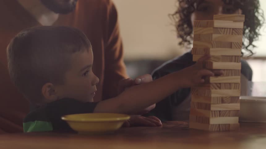 A father and his sons are playing jenga at a table in their home