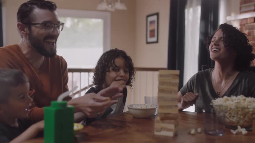 A family sits at a table playing a game and eating popcorn