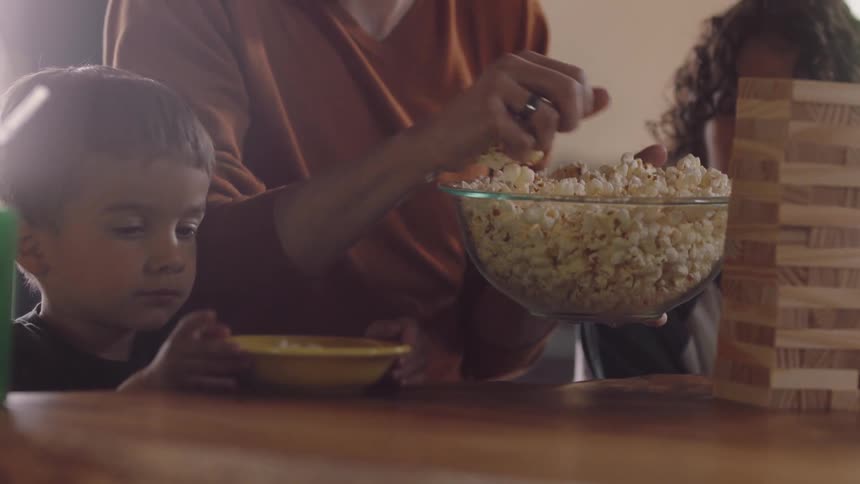 Mother puts popcorn in bowl for their children while playing jenga at table