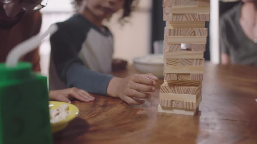 Boy trying to remove a piece from a jenga tower while their parents watch