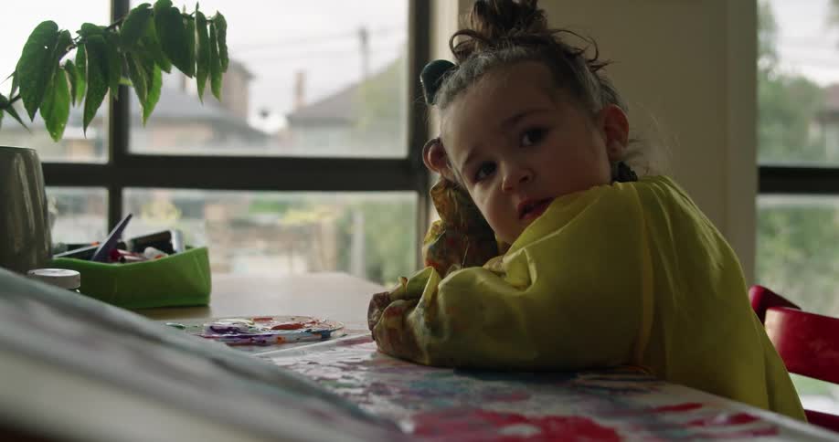 A little girl is sitting at a table talking and pointing to her activity