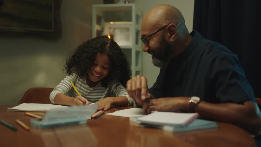 Father helps daughter with homework while sitting on the dinning table at home