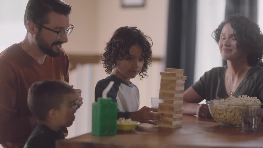 A family sits at a table talking as they play jenga and eat popcorn