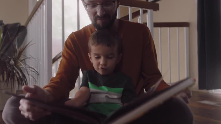 Father and son sit onground near staircase looking through books