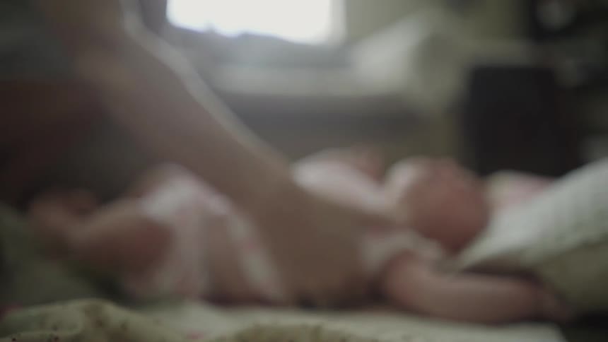 A person picks up a baby from a bed