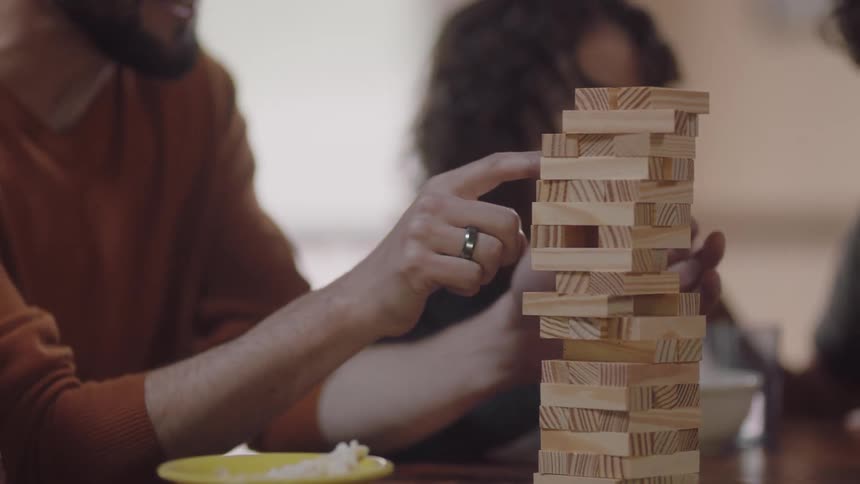 A family of four are playing a game with wood blocks on a table in their home during the day