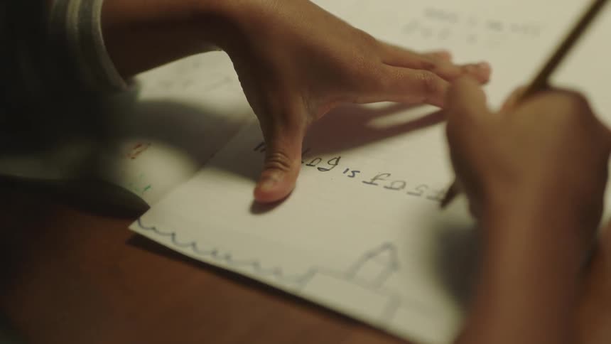 A child is writing on paper with a pencil