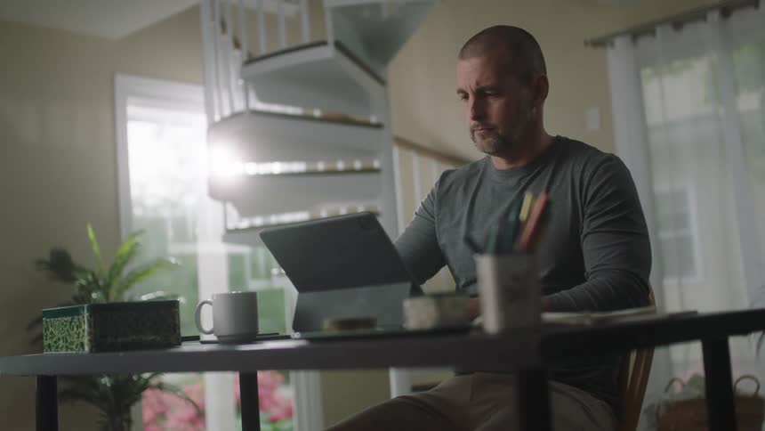 A man uses his laptop at home near a spiral staircase