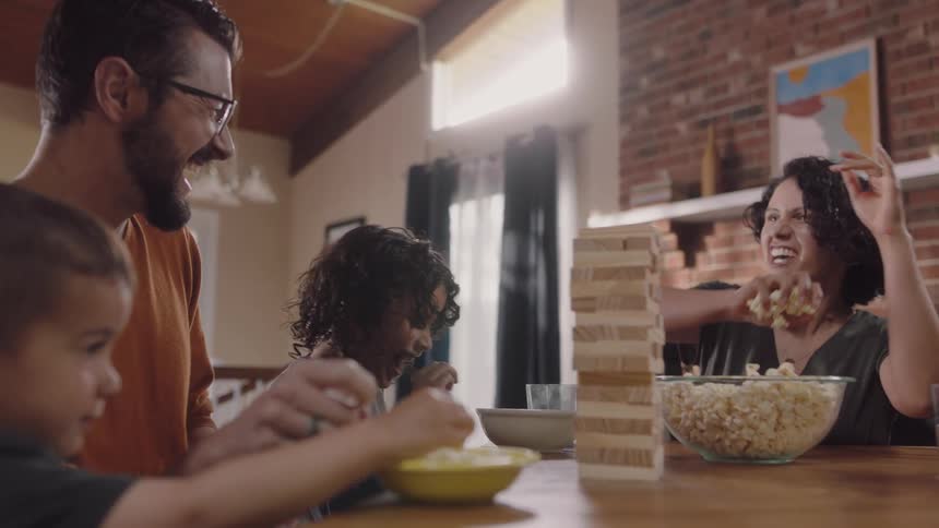 A woman throws handfuls of popcorn at her husband and sons as they play a game at home