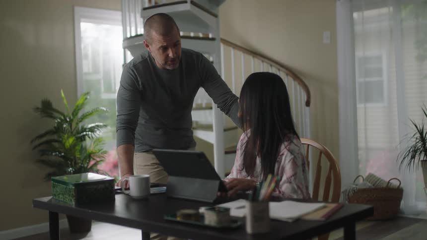 A man walks over to a woman sitting at a desk working and leans forward to talk