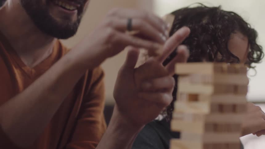 A man laughs as he places a piece on a jenga game he is playing with his son
