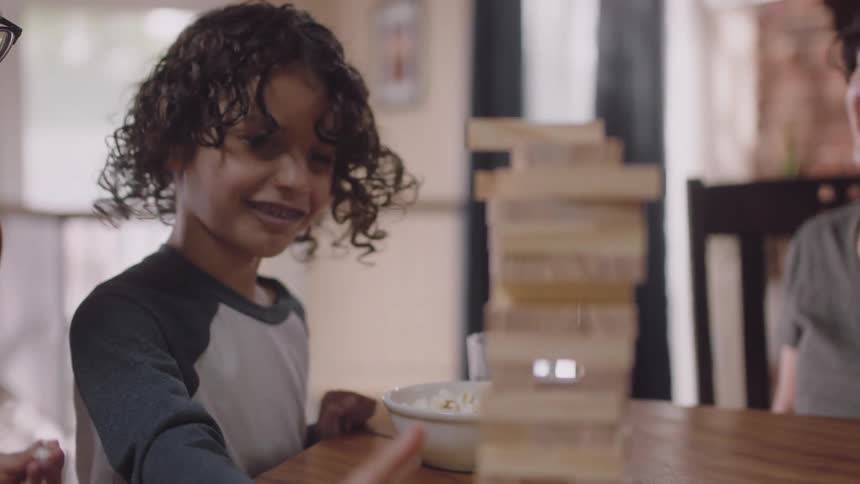 A woman laughs and shakes her finger at her son who shakes his head no as he is about to pull out a jenga piece in a game they are playing