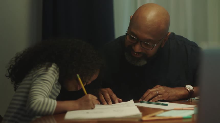 Man helps her daughter with homework while sitting in the dinning room at home