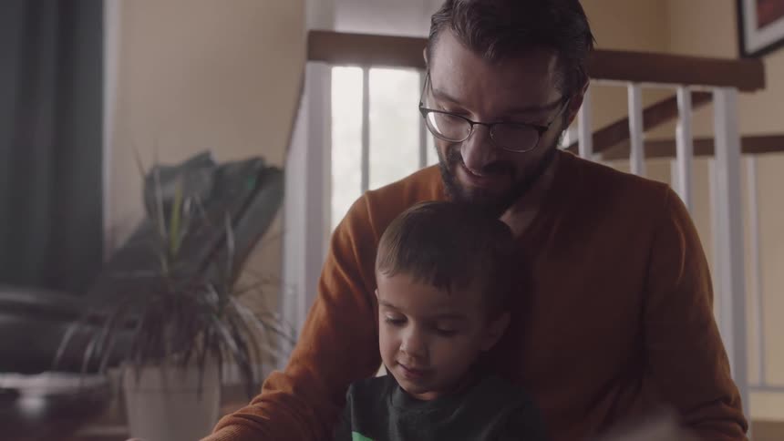 A boy sits in his fathers lap as they read a book together